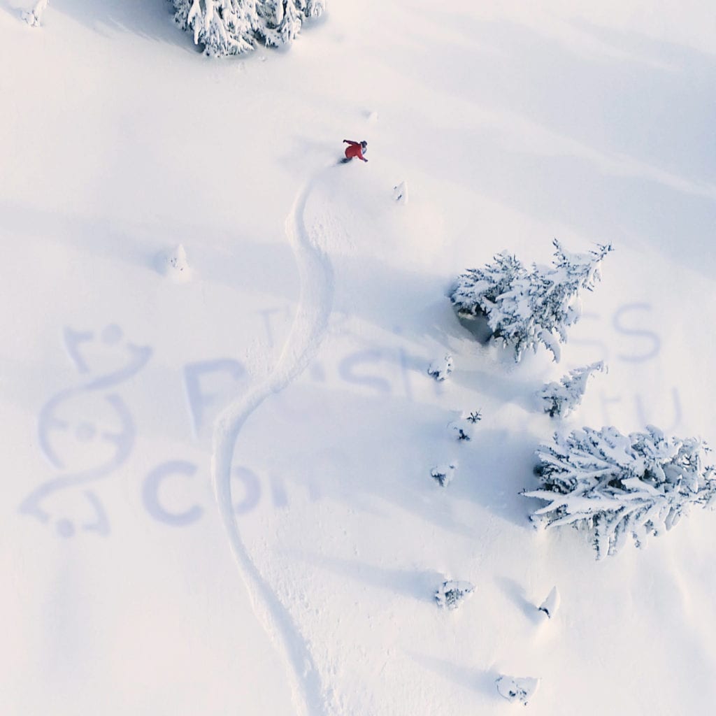 Aerial 'logo teaser' showing a snowy landscape with the logo partially carved into the snow