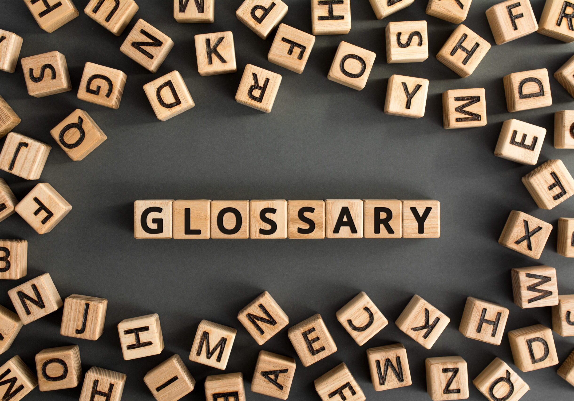 Glossary - word from wooden blocks with letters, alphabetical list with words meanings dictionary glossary  concept, random letters around, top view on grey background